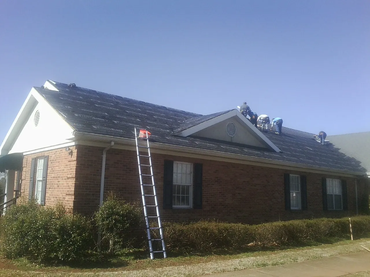 Crew tearing shingles off a brick ranch roof with a ladder set — Metal Roof Repair work by our crew in West Islip