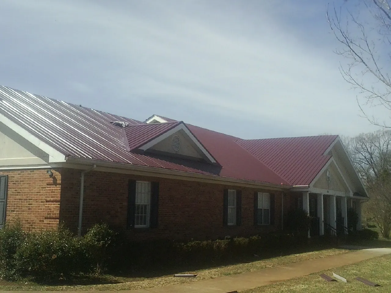 Red metal roof with gabled entries on a long brick building, from a Hail Damage Roof Repair job in West Islip