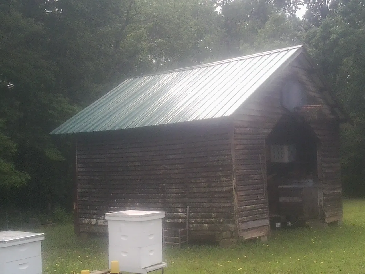 Green metal roof on a weathered barn beside stacked beehives in West Islip