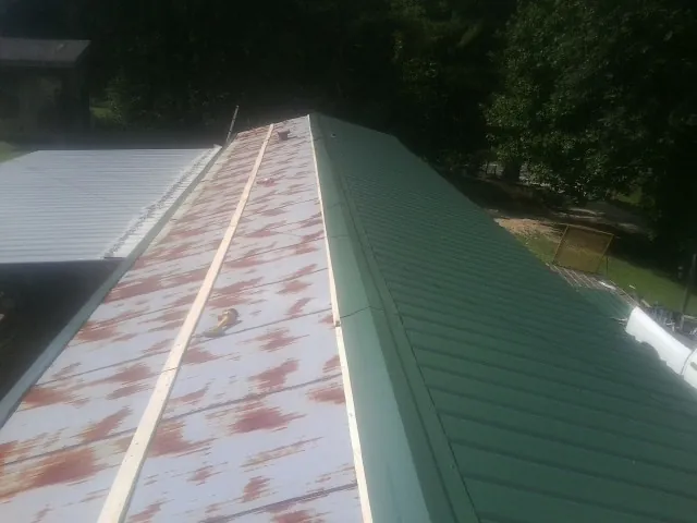 Old rusted panels beside newly installed green metal roofing — Wind Damage Roof Repair by Roofing Brothers in West Islip
