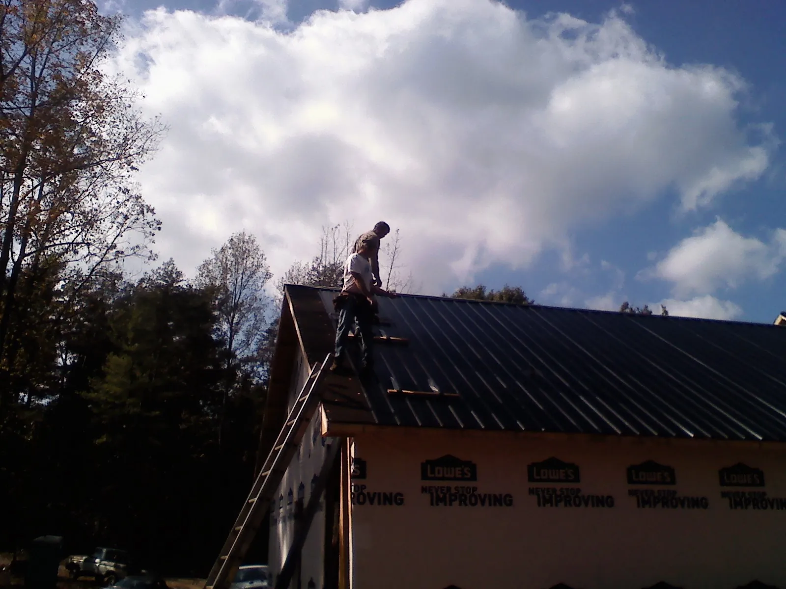 Roofer fastening dark metal panels high against a cloudy sky, from a Roof Inspection job in West Islip