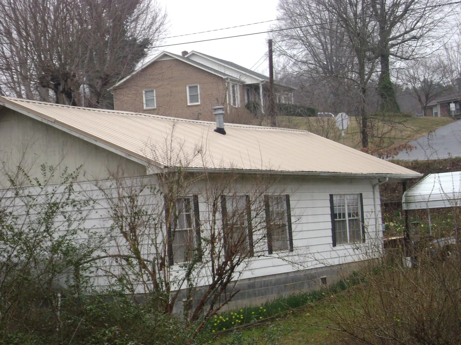 Tan metal roof on a white sided house set into a hillside — Commercial Roofing by Roofing Brothers in West Islip